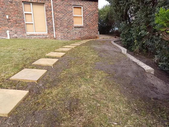 A new paver path laid across a lawn beside a brick house