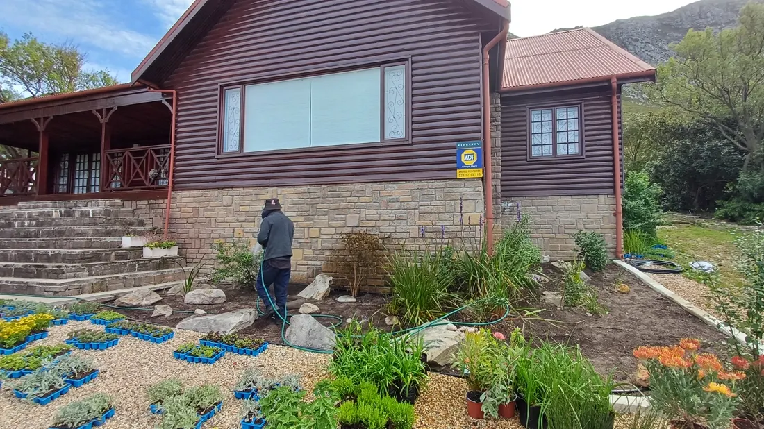 A gardener planting a bed beside a timber house with stone steps
